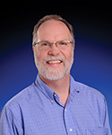 Photo of Dr. Irwin. White man middled aged man, with a white beard smiling.