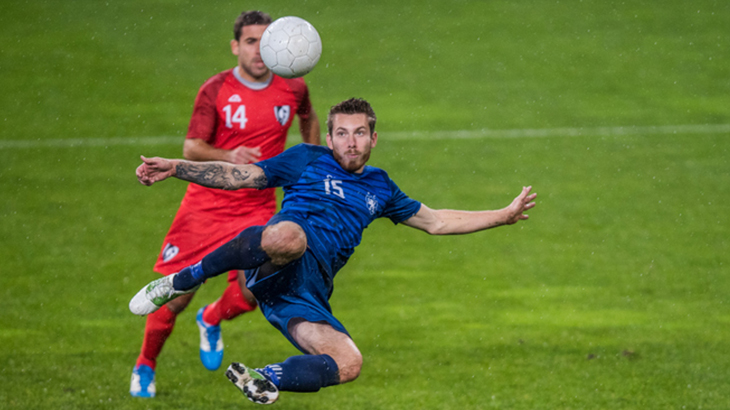 Male football player kicking football in air on field during match