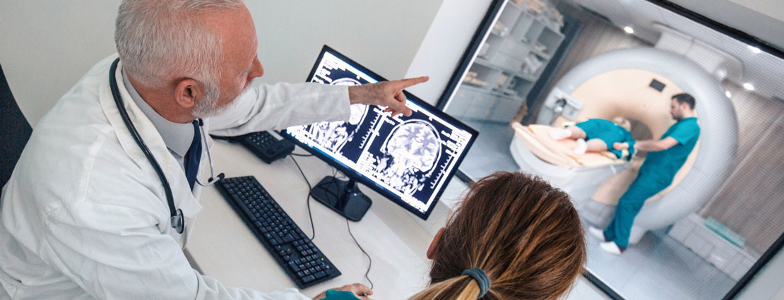 doctor and nurse in front of a computer monitor in view of patient getting an MRI