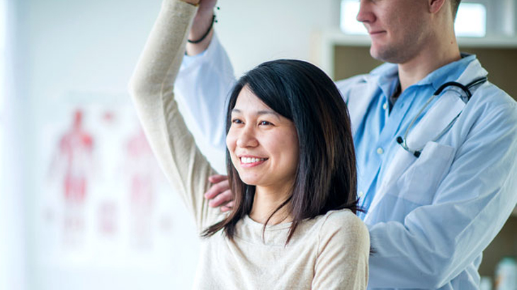 Smiling woman has her shoulder assessed by physician