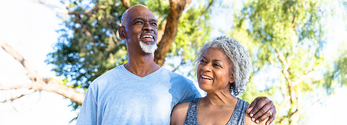 A healthcare provider holds a stethoscope on the back of an older female patient to listen to her breathing. Both women are wearing masks.