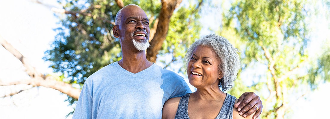 A healthcare provider holds a stethoscope on the back of an older female patient to listen to her breathing. Both women are wearing masks.