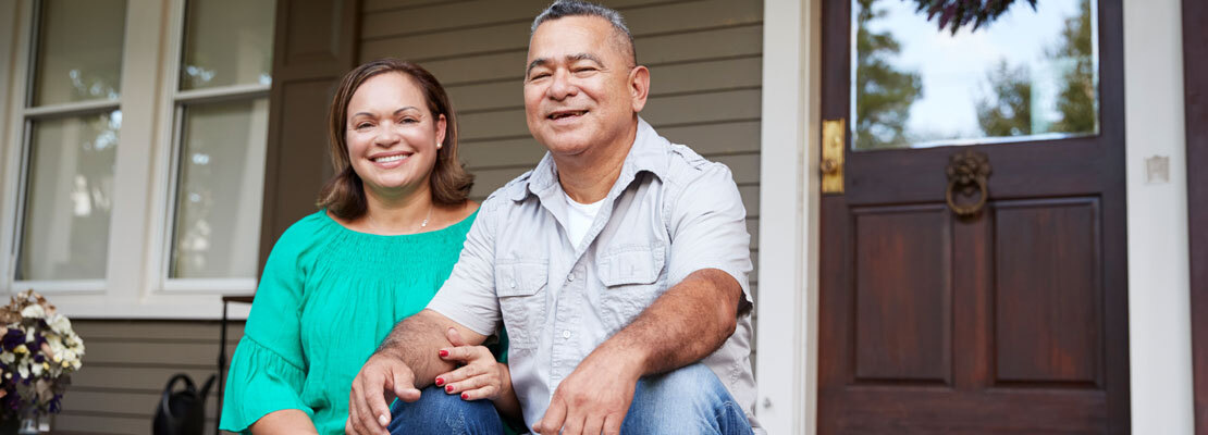 A healthcare provider holds a stethoscope on the back of an older female patient to listen to her breathing. Both women are wearing masks.