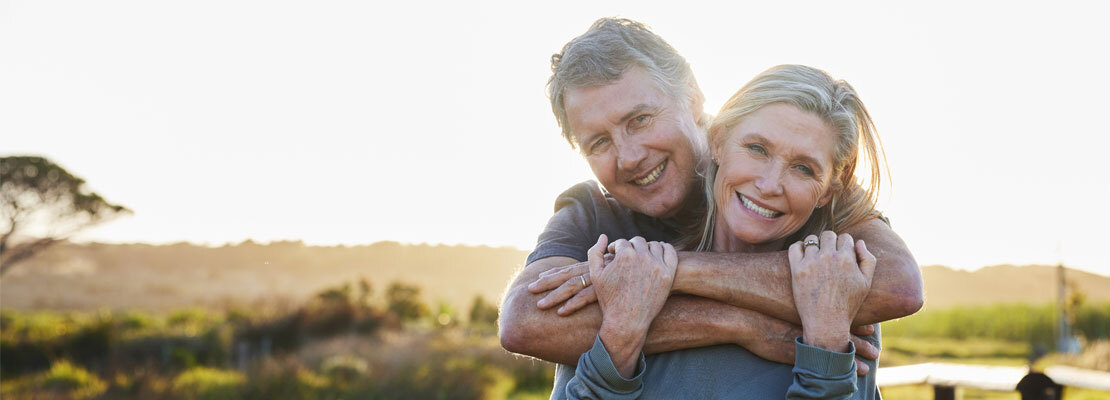 A mature African American couple smiles and laughs as they walk off of a tennis court outdoors.
